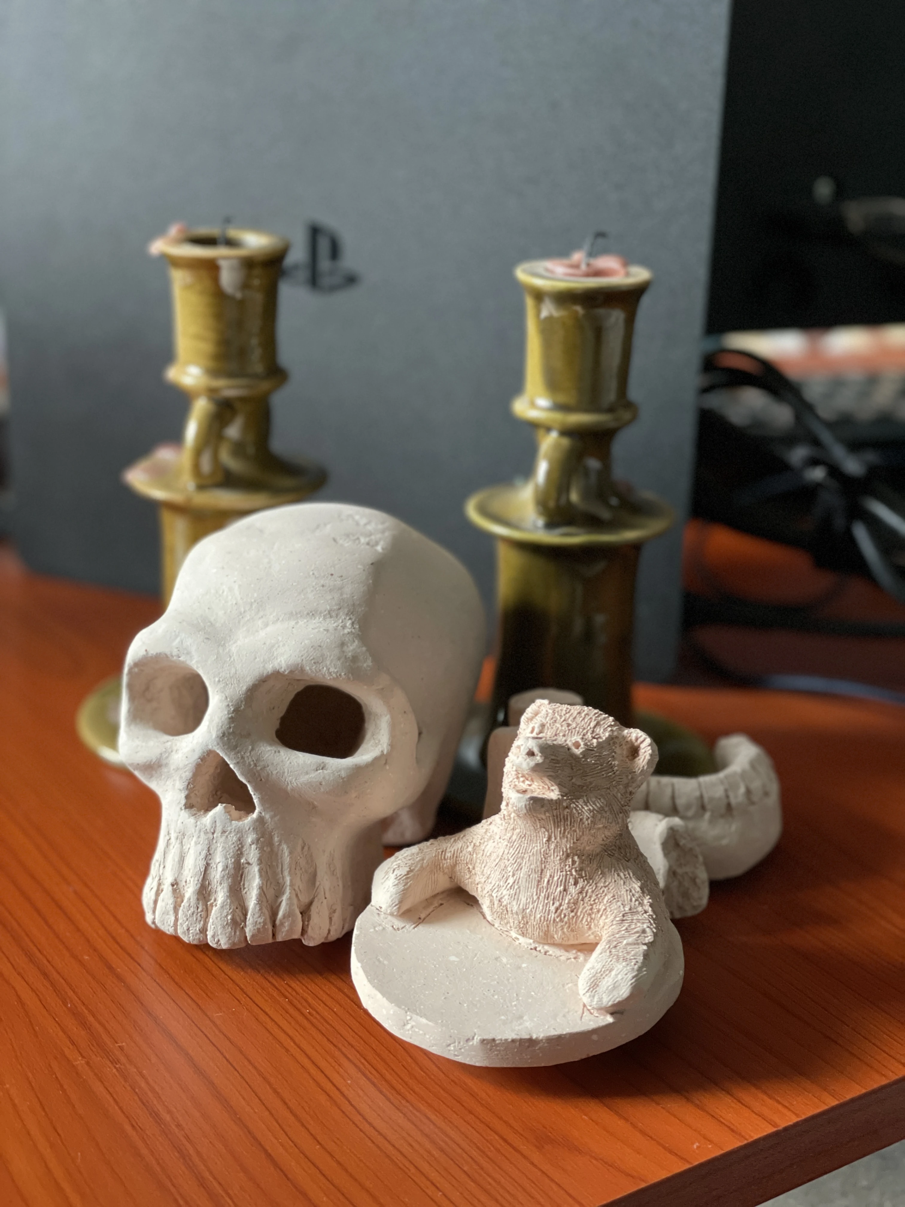 Sculpt of a skull without jaw and a sculpt of a bear as part of a cup lid with both arms lying on the lid and his mouth open. They don't have paint.